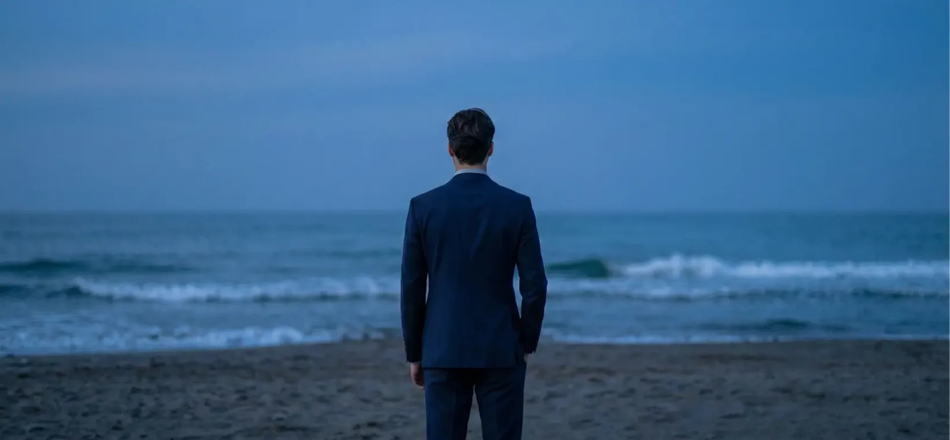 Patrick Liverani di spalle, in riva al mare, guarda l’orizzonte